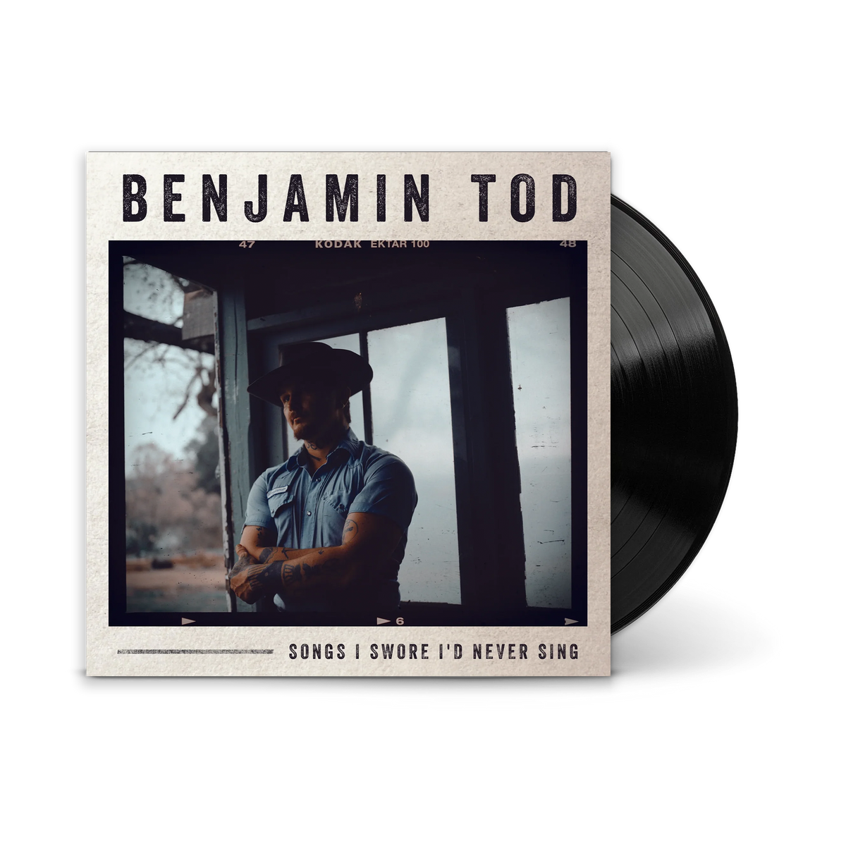 A vinyl record partially pulled from its album cover. The cover reads 'BENJAMIN TOD' and 'SONGS I SWORE I'D NEVER SING,' with a photo of a man in a cowboy hat by a window.